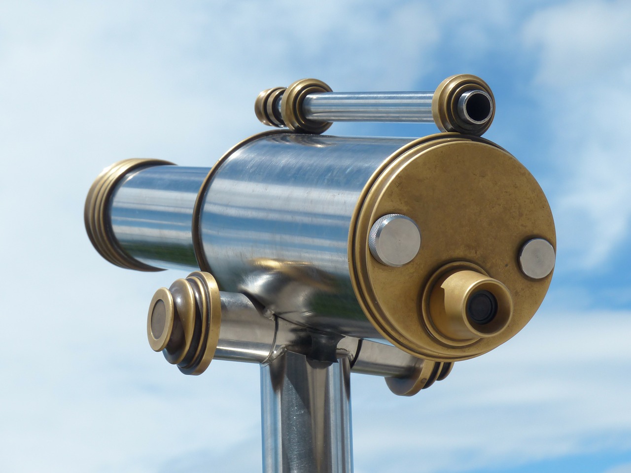 a picture of a gold and silver telescope with blue sky with clouds behind it