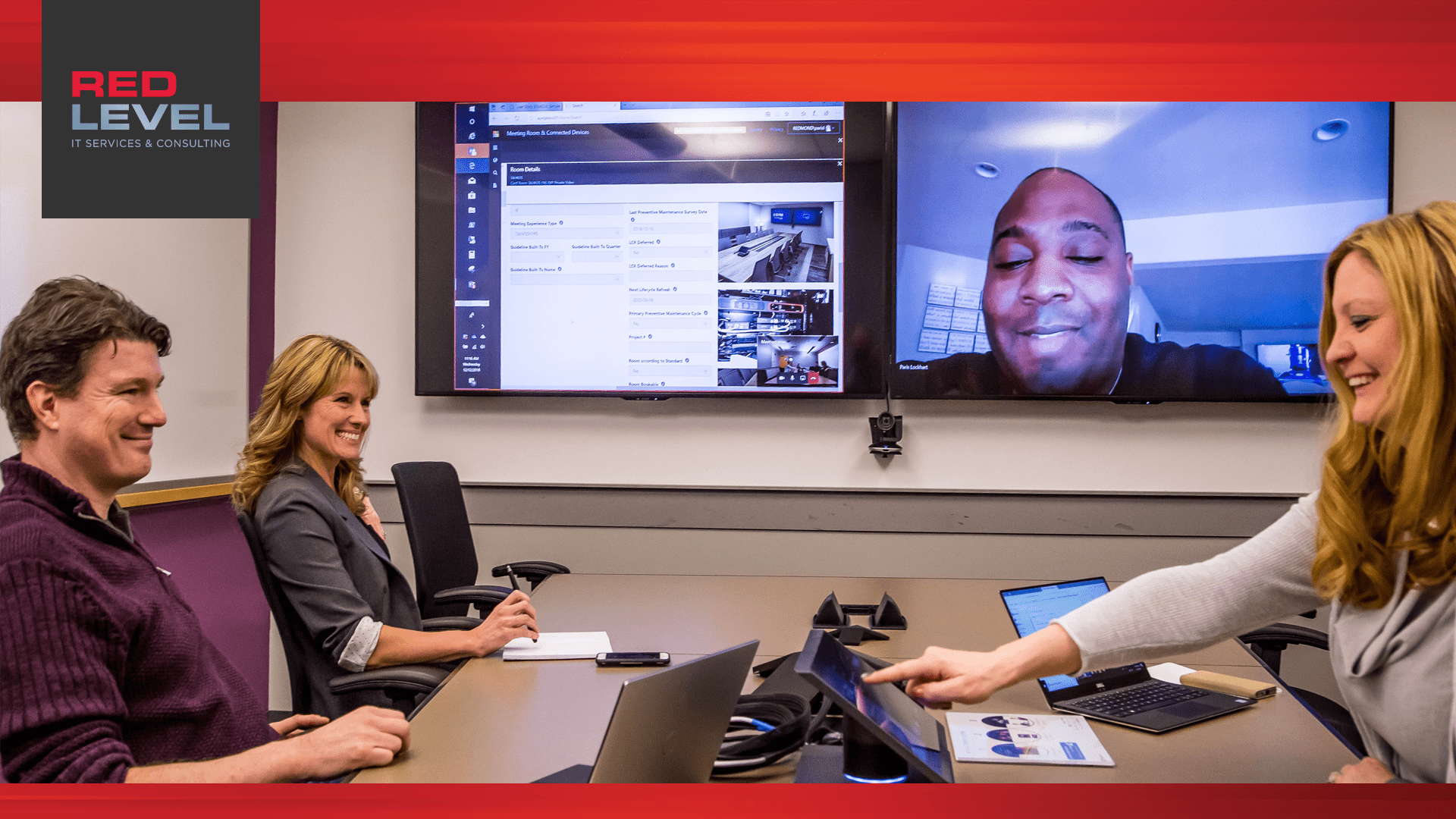 smiling people in a conference room talking to someone on a screen displaying a hybrid workplace
